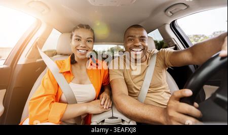 Ein junges afroamerikanisches Paar, das in einem Auto in die Kamera schaut und hell lächelt Stockfoto