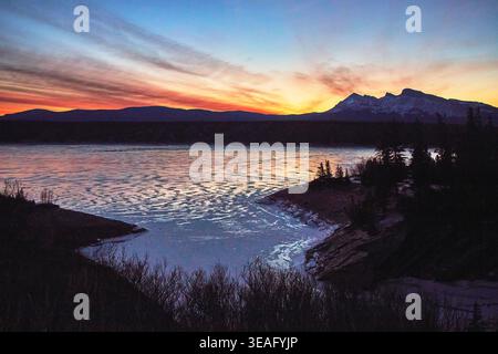Frozen Lake Sunset mit Winter Mountains und Silhouette Bäume Stockfoto