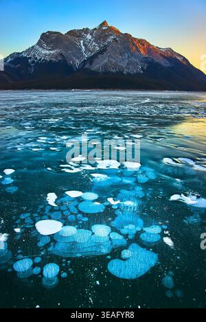 Frozen Lake Ice Bubbles und Snow Capped Mountain bei Sonnenaufgang im Winter Stockfoto