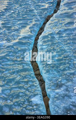 Cracked Blue Ice Sheets und Rocky Ground Winter Texture auf dem gefrorenen See Stockfoto