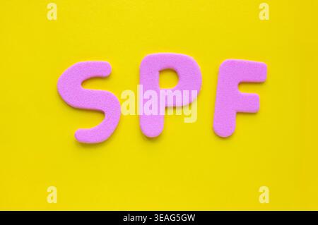 Pinkfarbene Buchstaben SPF auf hellgelbem Hintergrund, minimale flache Komposition mit Kopierraum. Farbenfrohes Sommerkonzept, das den Sonnenschutz repräsentiert Stockfoto
