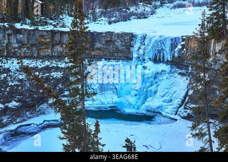 Gefrorener Wasserfall und Icy Pool mit Cliff Face und Evergreens in der Winterlandschaft Stockfoto