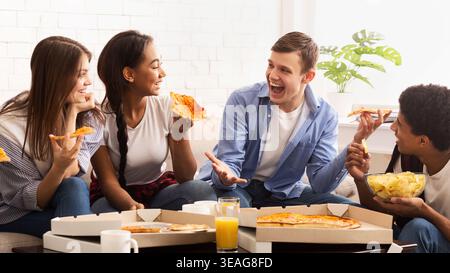 Freunde genießen gemeinsam Pizza in einem gemütlichen Wohnzimmer während einer Abendveranstaltung Stockfoto