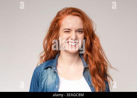 Eine junge Frau in einem Denim-Shirt mit langen, welligen Haaren zwinkert und lächelt Stockfoto