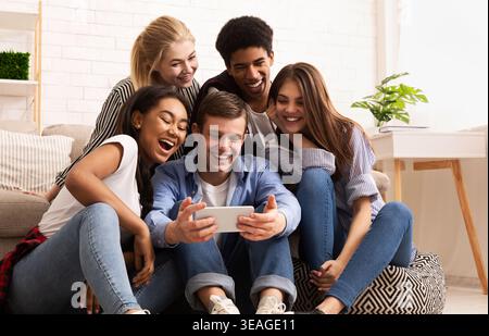 Freunde genießen einen lustigen Moment zusammen, während sie sich etwas auf einem Smartphone im Haus ansehen Stockfoto