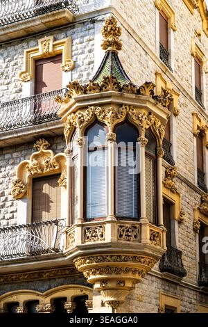 Verzierte historische Steinbauecke mit dekorativem Erkerfenster, goldenen Zierleisten, schmiedeeisernen Balkonen und geschlossenen Fensterläden bei warmem Sonnenlicht, EU Stockfoto
