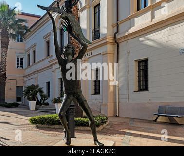 Bronzestatue einer Figur mit einem Vogel steht auf einem gepflasterten platz bei der Biblioteca Comunale in Olbia, Sardinien, unter hellem Tageslicht. Stockfoto