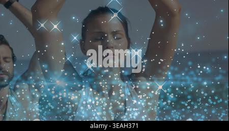 Eine Frau, die im Tank Yoga im Studio macht, mit blauen Bokeh-Funkeln und Armband Stockfoto