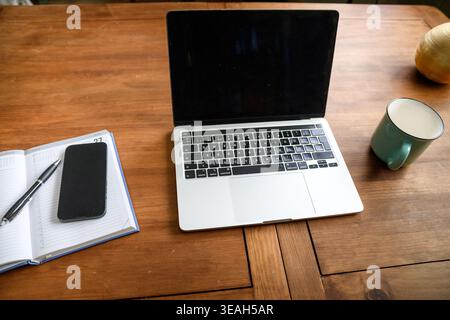 Draufsicht auf den Schreibtisch im Heimbüro mit Laptop, Notebook, Telefon und Kaffee, minimaler Fernzugriff. Stockfoto