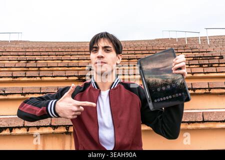 Junger Mann, der ein Tablet hält, der in lässiger Pose zeigt Stockfoto