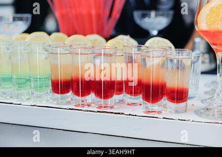 Bunte Cocktailaufnahmen Auf Reflektierender Arbeitsplatte Mit Zitronenscheiben, Klare Gläser Mit Rotem Bis Grünem Farbverlauf, Sirup Stockfoto
