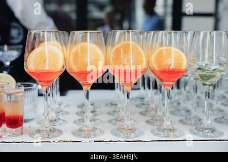Lebhafte Cocktails Mit Orangenscheiben Am Bartheken, Prickelnde Aperitif-Gläser In Reihe, Heller Farbverlauf, Sommerparty-Energie Stockfoto