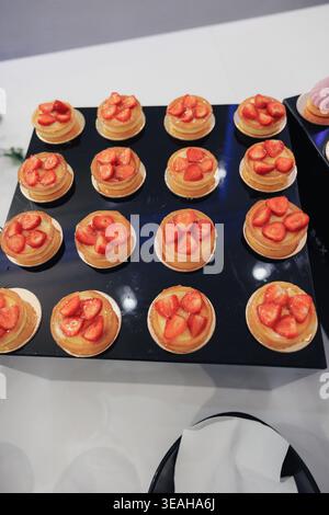 Mini-Erdbeertorten Auf Schwarzem Tablett, Bäckerei Bereitet Catering-Bestellung Vor, Goldene Krusten Gefüllt Mit Vanillesahne, Glasierte Erdbeerscheiben, Ordentliche Reihen Auf Stockfoto