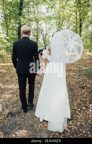 Braut Und Bräutigam Spazieren Durch Den Wald Mit Spitzenschirm, Kaukasisches Paar Auf Dem Intimen Elopement Path, Dappled Light, Rustikale Blätter Unter Den Füßen Und Stockfoto