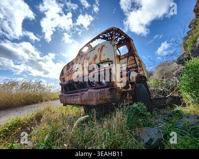 Altes verlassenes, verrostetes Fahrzeug. Rostiger, heruntergekommener Truck unter weißen Wolken und sonnigem Himmel. Schrott-Konzept Stockfoto