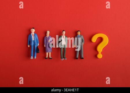 Gruppe von Miniaturpersonen neben einem gelben Fragezeichen auf rotem Hintergrund, die Auswahl, Entscheidungsfindung, Auswahlprozess und Unsicherheit in repräsentieren Stockfoto