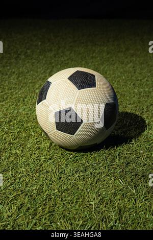 Der strukturierte schwarz-weiße Fußball liegt auf kurzem grünem Gras und wirft scharfe Schatten Stockfoto