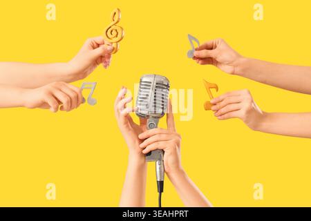 Weibliche Hände, die Retro-Mikrofon und Musiknotizen auf gelbem Hintergrund halten Stockfoto