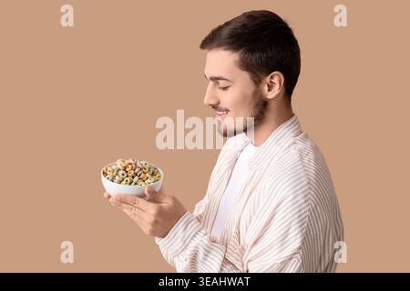 Schöner junger Mann, der eine Schüssel mit Müsliringen auf beigem Hintergrund hält Stockfoto