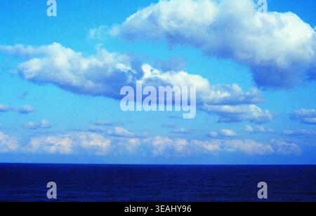 Ein riesiger, blauer Ozean erstreckt sich bis zum Horizont und trifft auf einen Himmel aus flauschigen weißen Wolken. Stockfoto