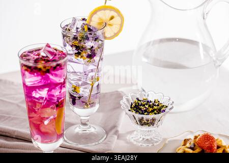 Ein Glas Eistee mit einer Zitronenscheibe und einer Waffel mit Erdbeere auf einer weißen Tischdecke. Stockfoto