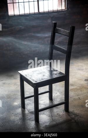 Ein abgenutzter, schwarzer Stuhl sitzt in einem schwach beleuchteten, verlassenen Industriebereich. Stockfoto