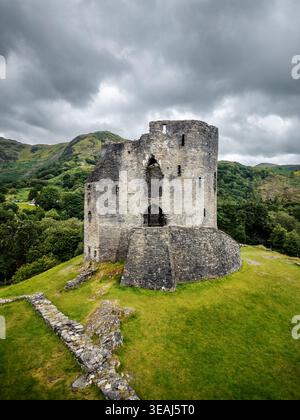Blick aus der Vogelperspektive auf den historischen Steinturm von Dolbadarn Castle, der auf einem grasbewachsenen Hügel inmitten üppiger grüner Berge unter einem bewölkten Himmel in Llanberis steht. Stockfoto