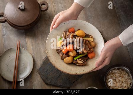 Hände halten eine Schüssel mit kurzes Rippchen im koreanischen Stil 'Galbijjim' auf einem Holztisch. Stockfoto