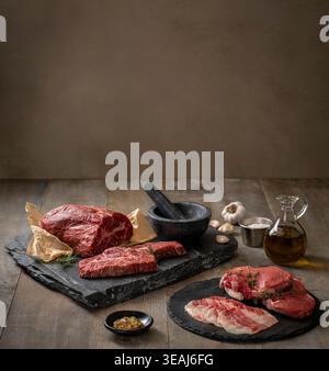 Auf einem rustikalen Holztisch stehen eine Auswahl an rohem Fleisch und Zutaten, darunter Steak, Rindfleisch und Gewürze. Stockfoto
