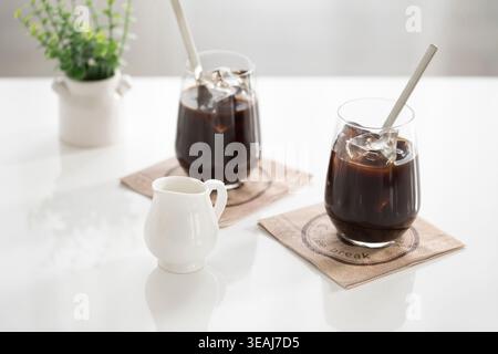 Zwei Gläser Eiskaffee auf einem weißen Tisch, mit einer kleinen Kaffeekanne im Vordergrund. Stockfoto
