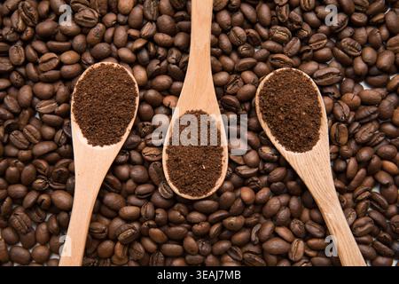 Drei mit Kaffeesatz gefüllte Holzlöffel sitzen auf einem Bett mit Kaffeebohnen. Stockfoto