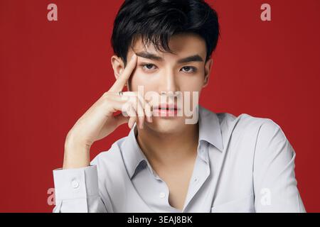 Ein junger asiatischer Mann sitzt im Profil, seine Hand auf seinem Tempel, in einem ruhigen, introspektiven Moment. Stockfoto