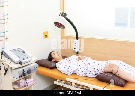 Eine Frau liegt auf einem Krankenhausbett und erhält eine elektrische Behandlung am Bein. Stockfoto