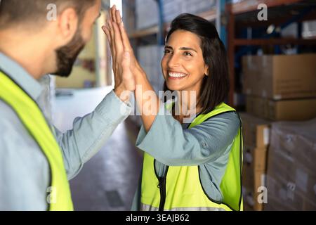 Latina-Arbeiterin High Five mit Kollegin im Lager Stockfoto