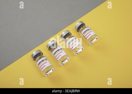 Vier leere COVID-19-Impfstofffläschchen auf gelbem Hintergrund. Stockfoto