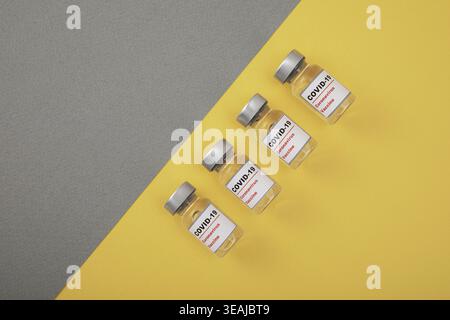Vier leere COVID-19-Impfstofffläschchen auf gelbem und grauem Hintergrund. Stockfoto