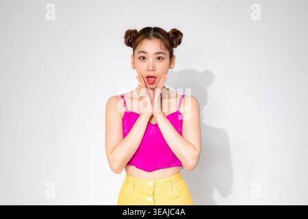 Eine junge Frau mit einem überraschten Ausdruck, ihre Hände bedecken ihren Mund, vor weißem Hintergrund. Stockfoto