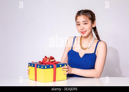 Eine junge Frau sitzt an einem Tisch und lächelt, während sie eine Geschenkverpackung hält. Stockfoto