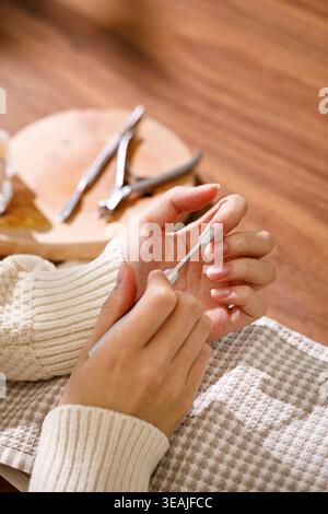 Eine Person schneidet ihre Fingernägel vorsichtig mit einem Nagelschneider auf einem Holztisch in einer ruhigen und ruhigen Wohnumgebung. Stockfoto