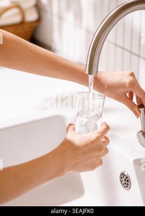 Eine Frau gießt Wasser aus einem Wasserhahn in ein Glas in einer modernen Küche. Stockfoto