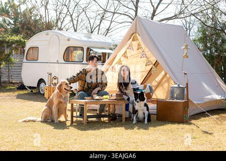 Ein junges Paar genießt ein Picknick mit ihren Hunden auf einem sonnigen Campingplatz. Stockfoto