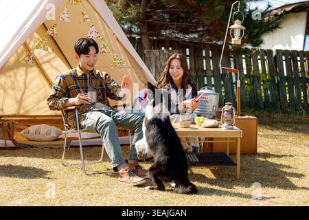 Ein Mann und eine Frau genießen ein Picknick mit ihrem Hund in einem sonnigen Hinterhof. Stockfoto