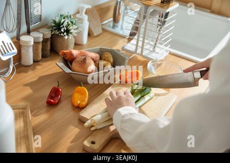 Eine Frau hackt Gemüse auf einer hölzernen Küchentheke. Stockfoto