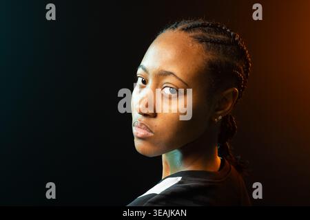 Afroamerikanerin im Studio posiert, Top mit weißem Streifen, Nieten, blaubrauner Felgenbeleuchtung Stockfoto