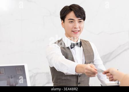 Ein lächelnder junger asiatischer männlicher Hotelrezeptionist überreicht einem Gast eine Schlüsselkarte. Stockfoto