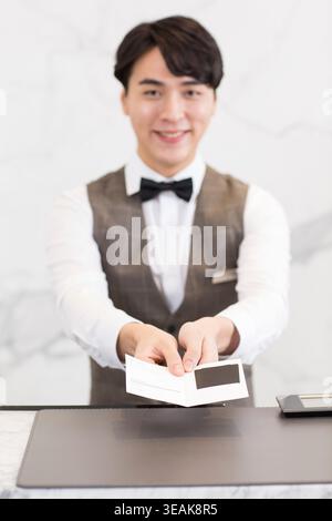 Ein Hotelrezeptionist überreicht einem Gast eine Schlüsselkarte in einer modernen Lobby. Stockfoto