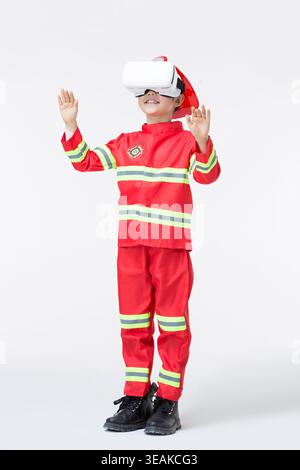 Ein Junge im Feuerwehrkostüm nutzt ein Virtual-Reality-Headset, um ein virtuelles Feuer zu erleben. Stockfoto
