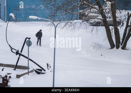Tallinn, Estland - 03. Januar 2025: Blick auf eine Einzelfigur, die sich der schneebedeckten Landschaft widersetzt, mit einem Ankerdenkmal, das in der wache steht Stockfoto