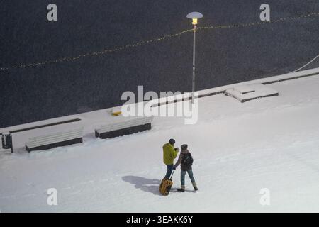 Tallinn, Estland - 03. Januar 2025: Blick auf zwei Figuren, die sich dem Schneesturm entlang der schneebedeckten Promenade trotzen, beleuchtet von einem einsamen Laternenpfahl, als Th Stockfoto