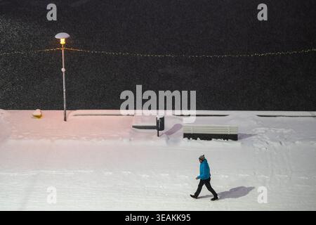 Tallinn, Estland - 03. Januar 2025: Blick auf eine Einzelfigur, die sich der verschneiten Uferpromenade widersetzt, das schlichte weiß im Kontrast zum dunklen Meer und dem warmen Glo Stockfoto